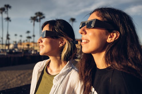 Two friends have fun together during a solar eclipse event. Their looking and pointing to the sun we...