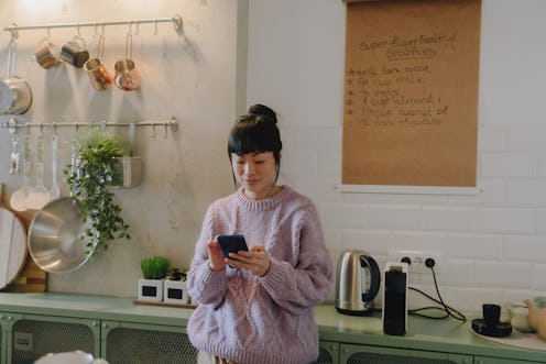 Photo of a Japanese woman using a smartphone in her kitchen.