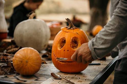 Family celebrating Halloween at home and preparing pumpkins. Creative girl making a Halloween decora...