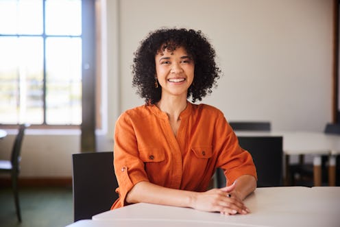 Portrait of a confident young businesswoman smiling while sitting along at a table in an open plan o...