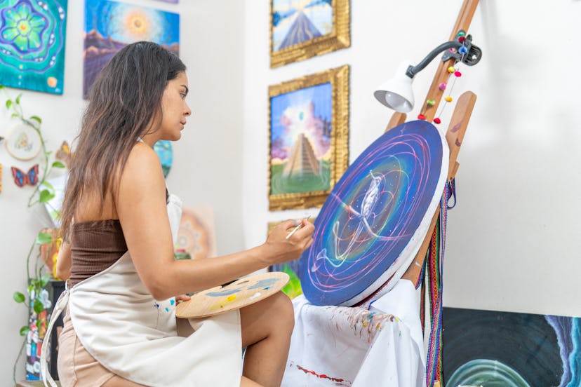 Young woman concentrating on painting a canvas with a brush, in her art studio.
