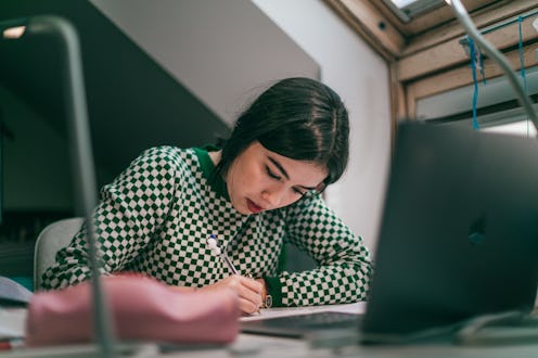 hispanic latina college student works on assignment in her dorm room.She is smiling and in the backg...