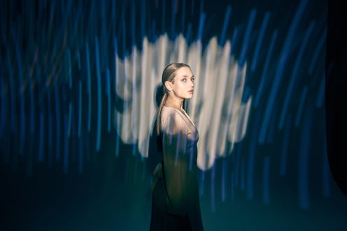 A young woman stands on a black background and looks away, waves of WiFi or wireless Internet pass t...