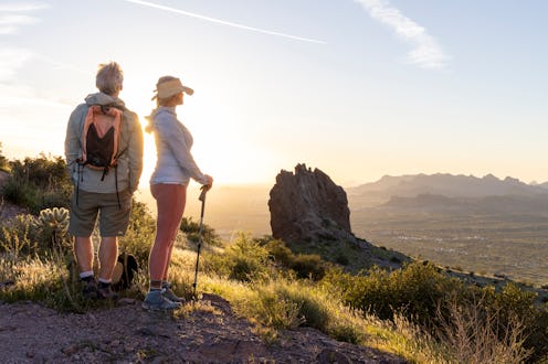Hiking couple pause to watch sunset over desert landscape and pinnacle