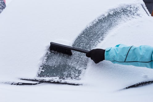 Woman cleaning snow from the car in the winter