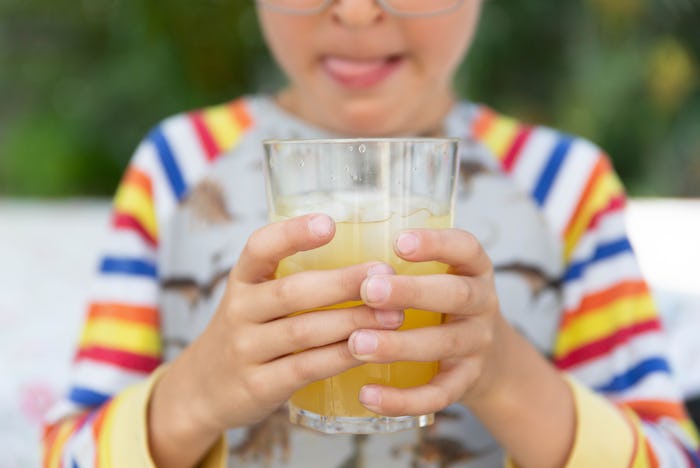 Boy holding glass of juice and licking lips with plants behind, in a story answering the question 'c...
