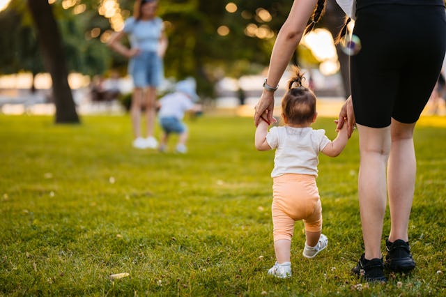 Beautiful young mother teaching her daughter how to walk in the park.