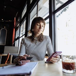 Female freelancer uses a phone and a notepad while working in a cafe, focused at work