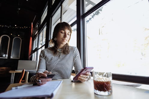 Female freelancer uses a phone and a notepad while working in a cafe, focused at work
