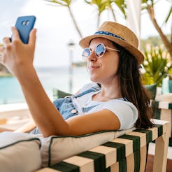 Relaxed young woman taking selfies at a seaside café in Parga, Greece.