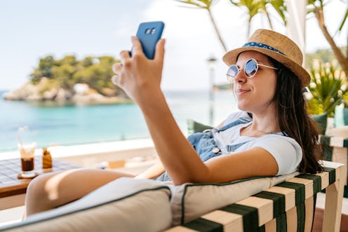 Relaxed young woman taking selfies at a seaside café in Parga, Greece.