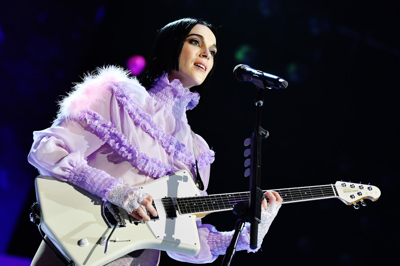 Female musician in a lilac ruffled outfit playing an electric guitar on stage.