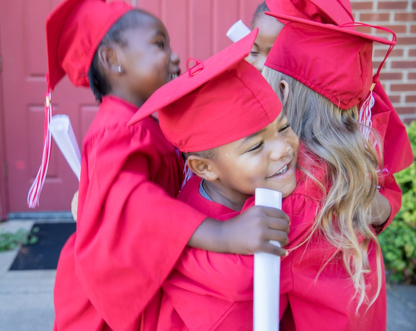 Diverse group of adorable preschool age children hug and jump after graduation at school