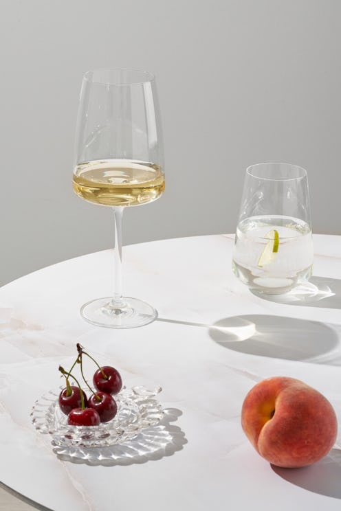 round coffee table with glass of white wine, glass of water with ice and lemon, and some fruit on sa...