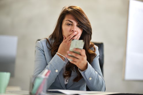 Young female entrepreneur reading a shocking text message on cell phone while working in the office.