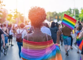 Rear view image of young African-American woman walking at the LGBTQI pride event and waving rainbow...