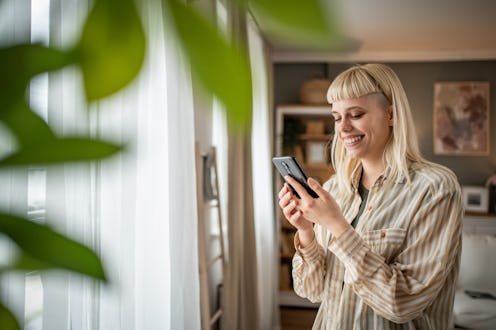 A young woman is enjoying a quiet morning in her apartment, using a mobile phone
