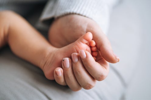Macro photo of mother holding leg of sleeping newborn 1 month baby boy with her hands