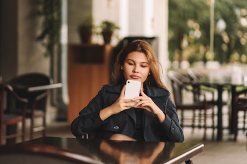A serious dissatisfied woman looks at her phone prints a text message using wireless technology and ...
