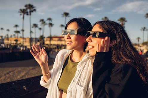 Two friends have fun together during a solar eclipse event. Their looking and pointing to the sun we...