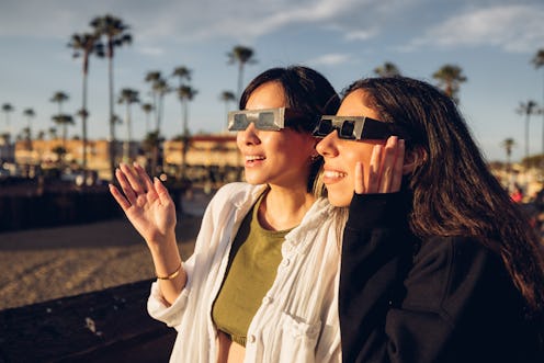 Two friends have fun together during a solar eclipse event. Their looking and pointing to the sun we...