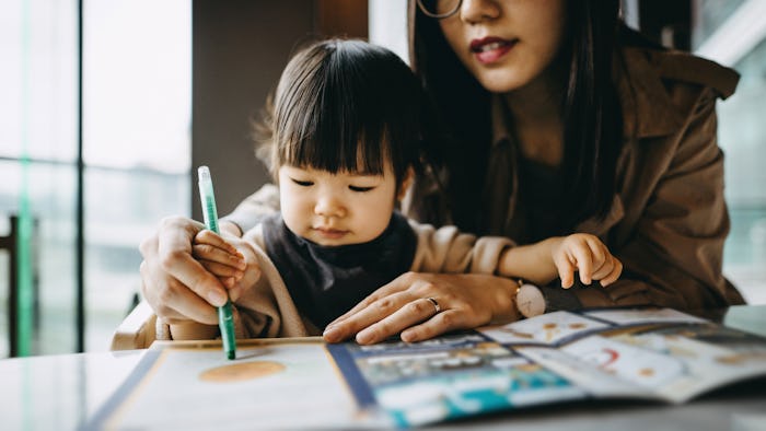 Young mother holding hand of cute infant daughter coloring, in a list of powerful baby girl names.