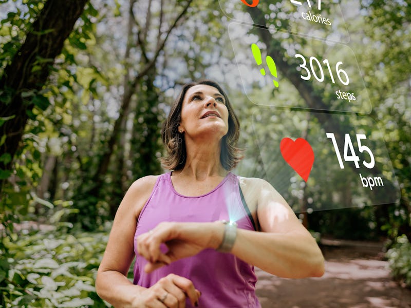 Mature woman with smart watch looking at sports infographic hologram on the public park