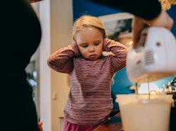 Mother doing cake with mixer while little girl covering her ears.