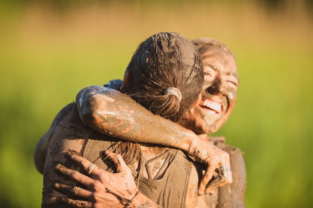 A female athlete is hugging her teammate at the end of their mud run competition. She is happy and s...