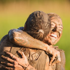 A female athlete is hugging her teammate at the end of their mud run competition. She is happy and s...