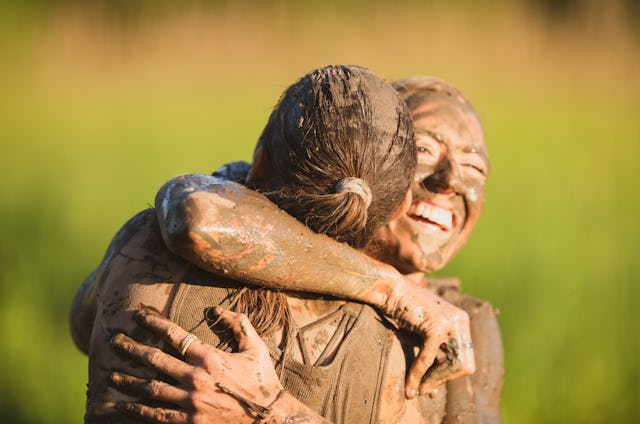 A female athlete is hugging her teammate at the end of their mud run competition. She is happy and s...