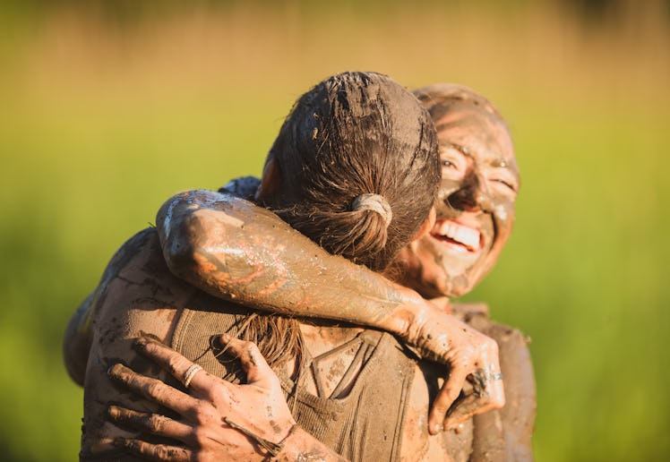 A female athlete is hugging her teammate at the end of their mud run competition. She is happy and s...