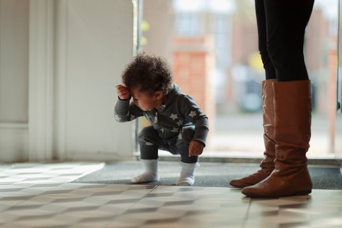 Cute baby girl in star pajamas crouching at front door in home entryway
