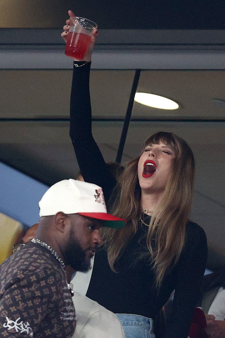 Taylor Swift holding up a red drink at the Kansas City Chiefs game against the New York Jets. 