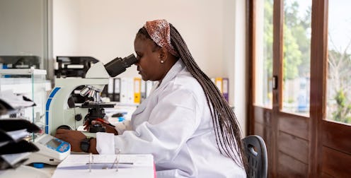 Side view of a woman technician in lab coat studying samples with microscope in pathology laboratory