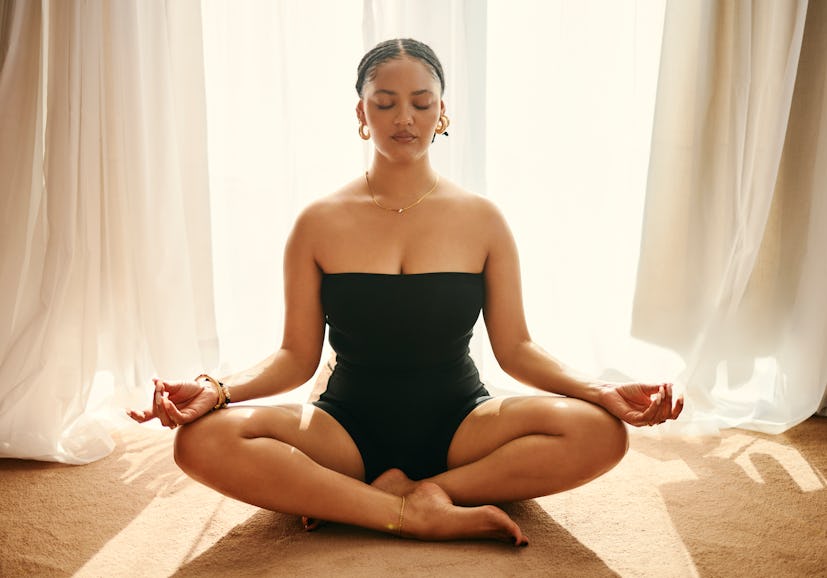 A woman sitting cross-legged meditating while she manifests with positive vibes quotes