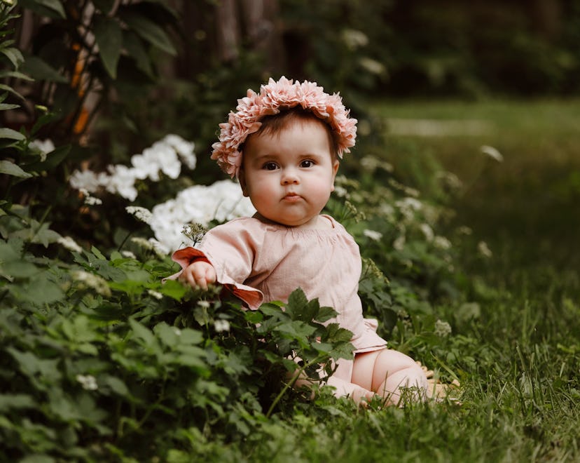 A beautiful baby girl, seven months old, sitting in a garden.