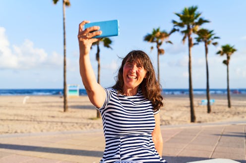 portrait of woman in casual clothes with her phone sitting on a bench on the beach looking away, fro...