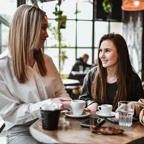Three women enjoying a conversation over coffee in a stylish café setting, with cups and a snack on …
