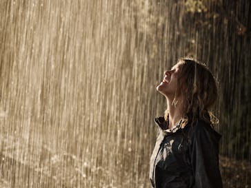 Happy woman in raincoat enjoying while standing on a pouring rain in nature. Copy space.