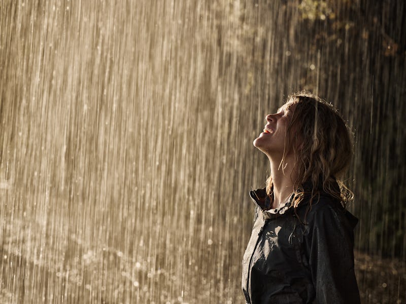 Happy woman in raincoat enjoying while standing on a pouring rain in nature. Copy space.