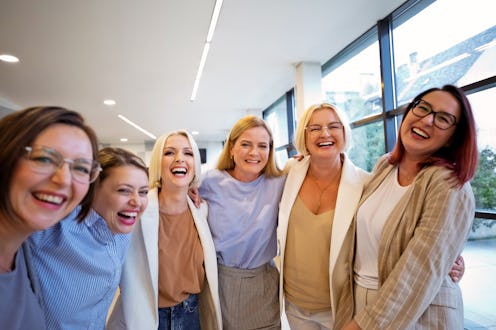 Portrait of cheerful female colleagues standing with arms around each other at office