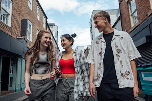 A low angle froint view of a group of three teenage friends walking through a side street on a summe...