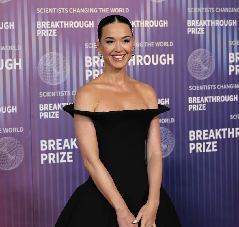 A woman in a black off-shoulder dress smiling at a Breakthrough Prize event, with a logo background.
