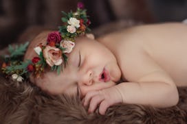 A portrait of a newborn baby girl sleeping on brown fur and wearing a flower crown.