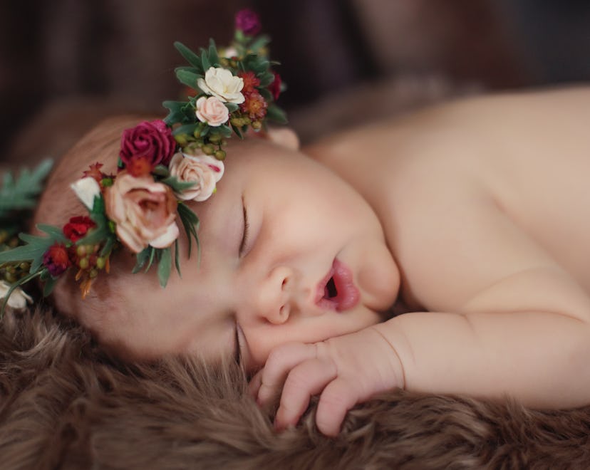 A portrait of a newborn baby girl sleeping on brown fur and wearing a flower crown.