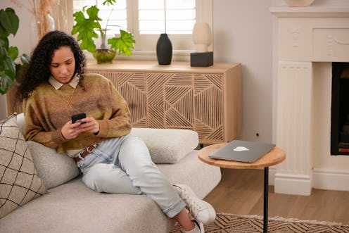 In the cozy living room, a woman holding her phone, as she explores the digital world from the comfo...
