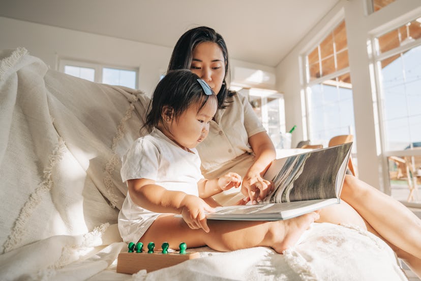 asian family sitting on bed and reading book at home, korean woman mother teaching little daughter t...