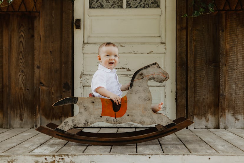 A one~year~old baby with a vintage boy name smiles at the camera as he sits on a porch in an antique...