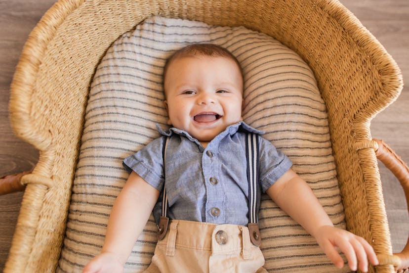 A baby with a vintage boy name wearing suspenders and laying in a basket, smiling at the camera.